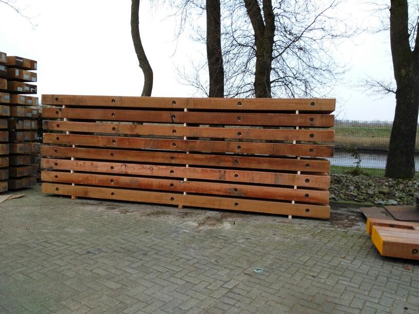 Gestapelde Basralocus schotten met bouten langs een sloot bij kale bomen