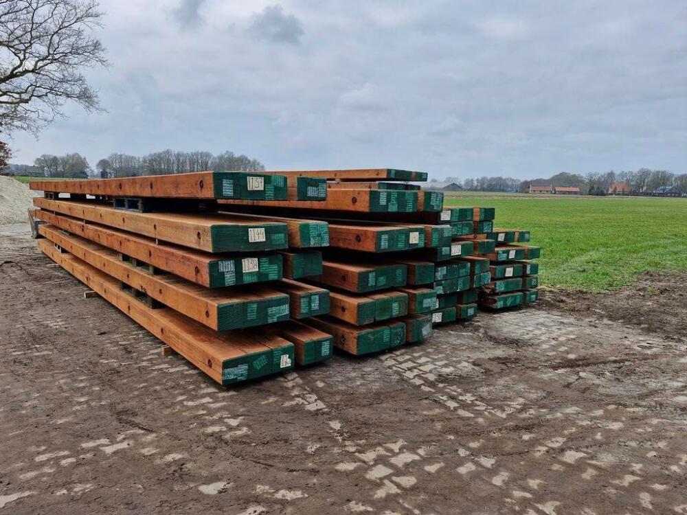 Meerdere stapels draglineschotten met groene uiteinden naast een weiland onder een bewolkte lucht